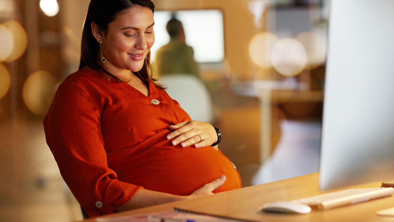 gestante sentada na cadeira com a mão na barriga prestes a entrar na licença-maternidade