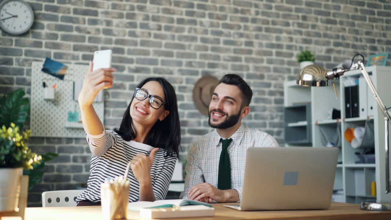 Duas pessoas sentadas em um ambiente com iluminação suave. Uma delas ajusta um smartphone em um tripé enquanto a outra organiza papéis, preparando a gravação de um conteúdo jurídico informativo. Imagem significando a representação de um Advogado Influencer.